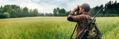 hunter in pasture looking through binoculars